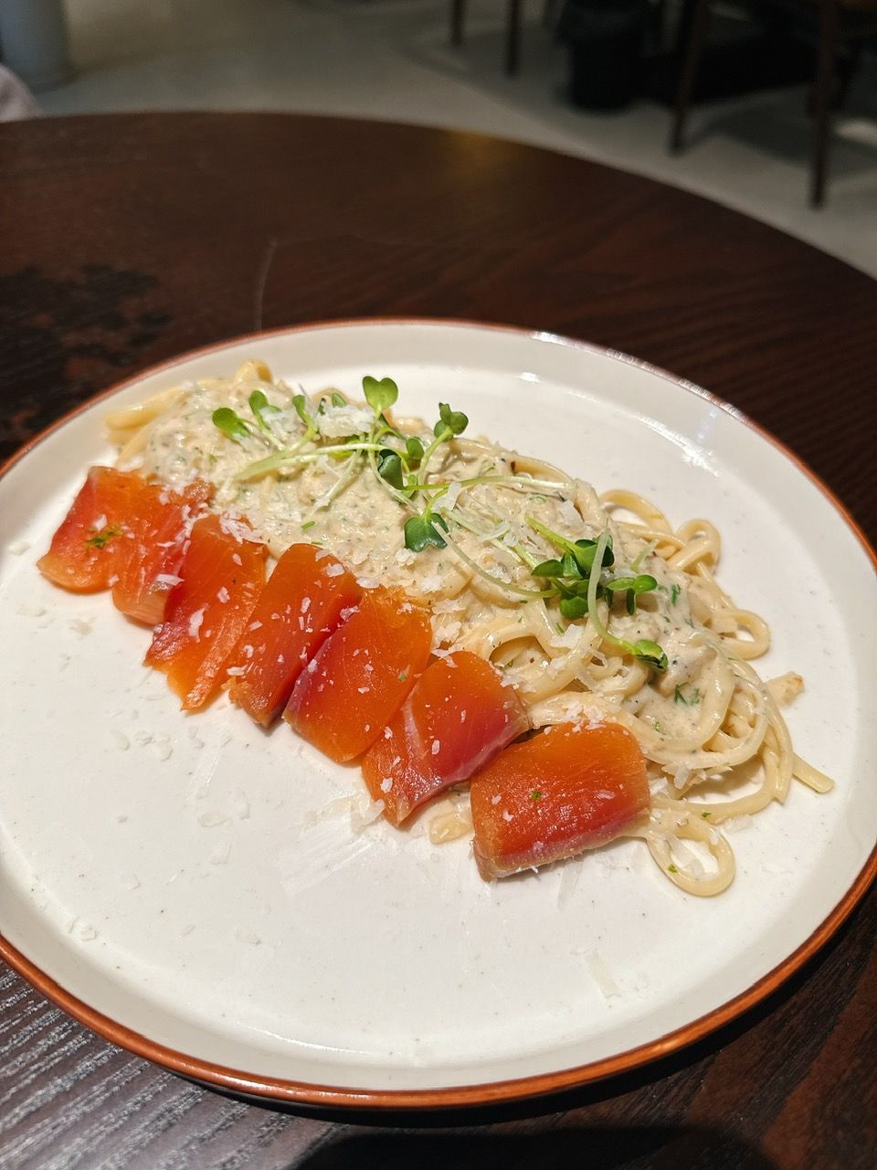 Een bord pasta met zalm en groenten, op een wit bord met een bruine rand.