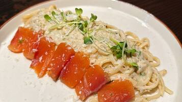 Een bord pasta met zalm en groenten, op een wit bord met een bruine rand.