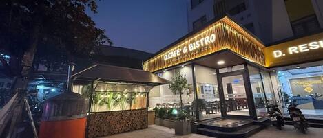 A cafe and bistro with outdoor seating, a pizza oven, and a building with a sign that reads "D. Residence".
