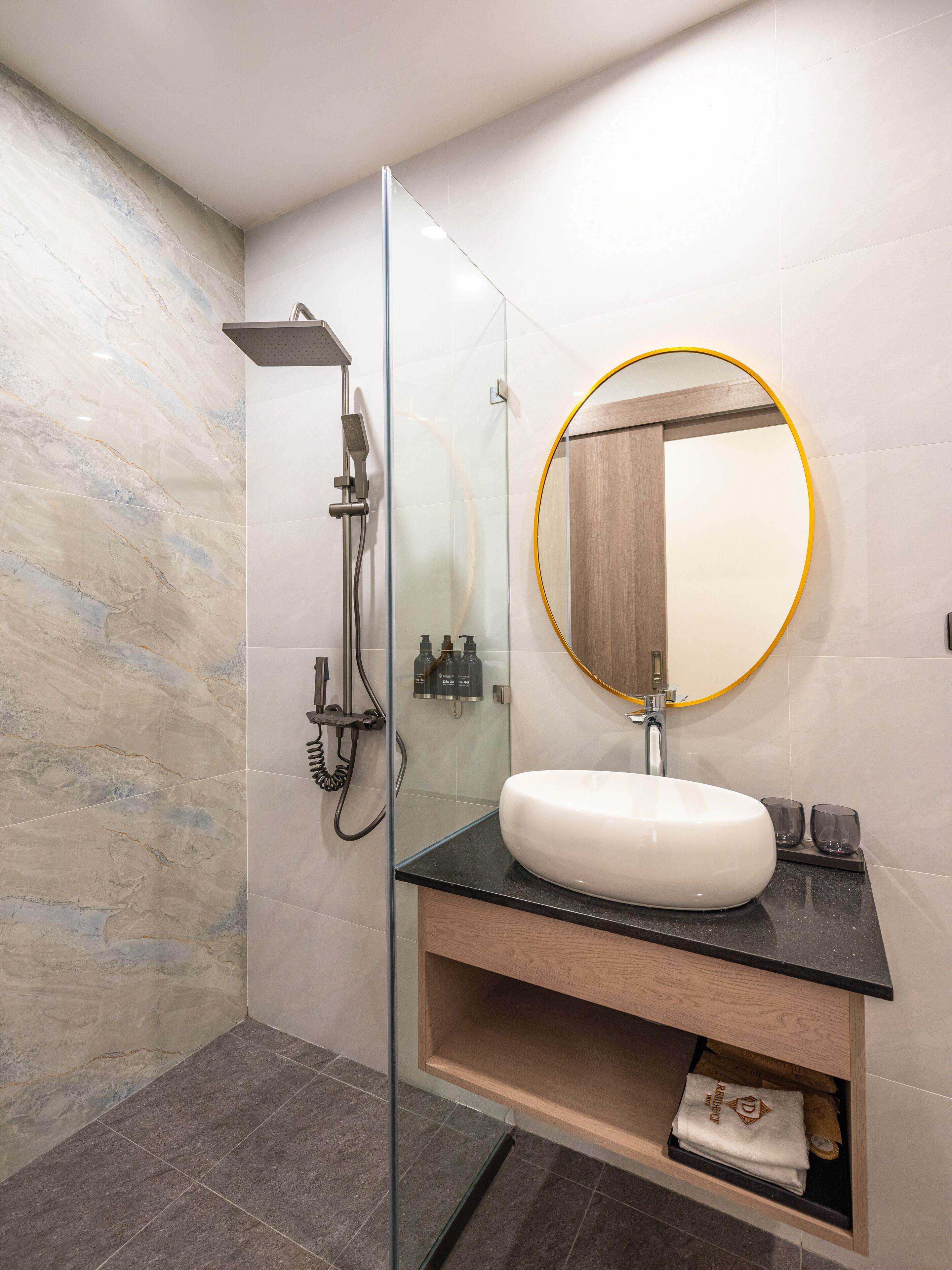 Une salle de bain moderne avec une douche à parois de verre, un lavabo blanc doté d’un plan de toilette noir et un meuble-lavabo en bois.