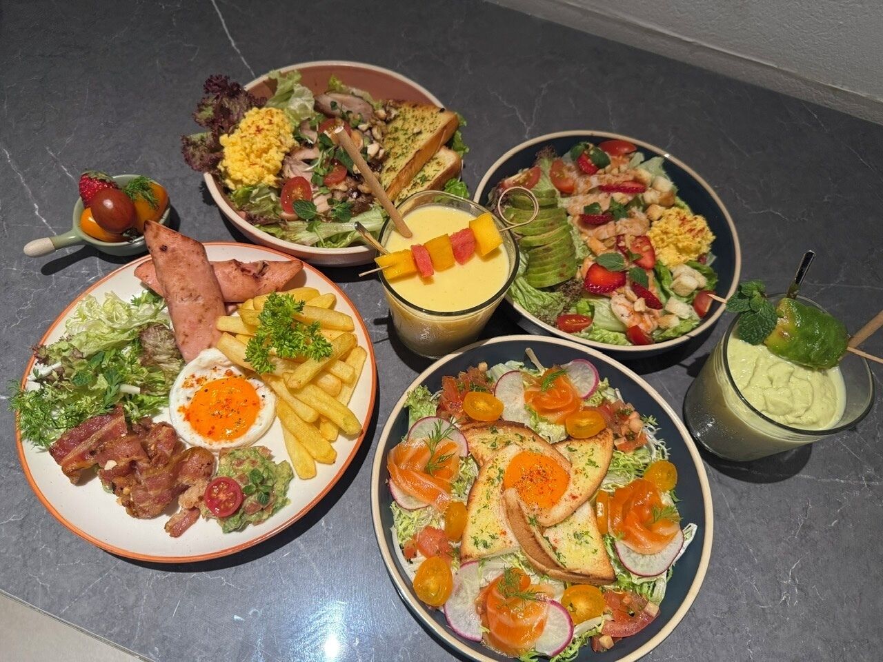 A variety of dishes including salads, eggs, and a drink on a table.