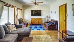 A living room with a sofa, two armchairs, a wooden cabinet, a blue rug, and a ceiling fan.