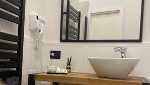 Un baño con tocador de madera, un lavabo blanco, un espejo, un secador de pelo y toallas.