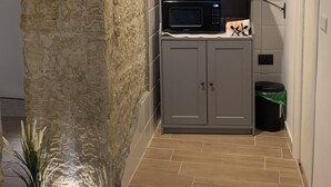 Una cocina con un revestimiento de piedra, una cafetera, un microondas y un pequeño cubo de basura.