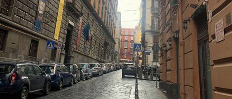 A narrow cobblestone street lined with historic buildings, some with balconies and signage.