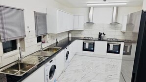 A modern kitchen with white cabinets, a black countertop, a built-in washing machine, and a gas stove. - Delightful Double En-suite Room (Ponders End)