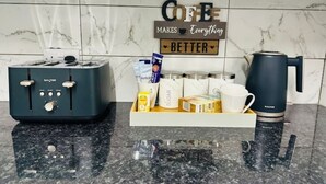 A kitchen counter with a coffee maker, a toaster, and a tray with coffee cups and sugar packets. - Delightful Double En-suite Room (Ponders End)