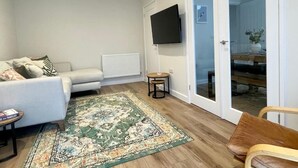 A living room with a sofa, a coffee table, a TV mounted on the wall, and a sliding glass door leading to a balcony.
