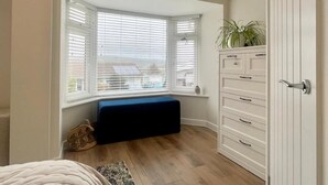 A bedroom with a bay window, a built-in bench, a dresser, and a potted plant.