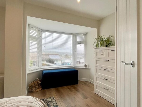 A bedroom with a bay window, a built-in bench, a dresser, and a potted plant.