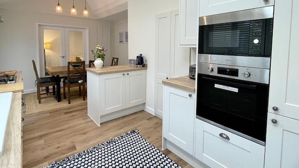 A modern kitchen with white cabinetry, a built-in oven, and a dining area with a wooden table and chairs.