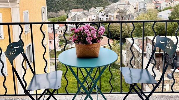 Ein Balkon mit Tisch und zwei Stühlen, mit Blick auf ein Dorf und Berge.