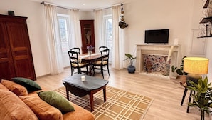 Ein Wohnzimmer mit einer Couch, einem Couchtisch, einem Esstisch mit Stühlen, einem Kamin, einem Fernseher und einer Topfpflanze.