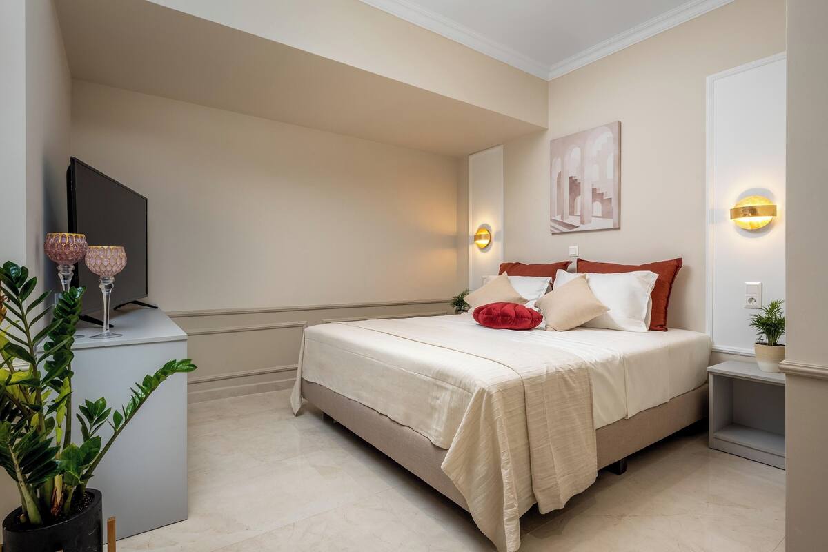 A neatly arranged bedroom with a bed, bedside tables, a TV, and wall-mounted lighting.