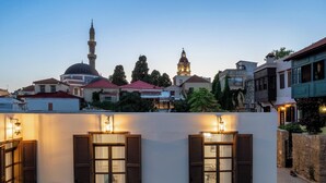A courtyard with a white wall, wooden shutters, and potted plants. - Alegrand Suites (Rhodes)