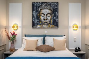 Un lit avec une couvre-lit bleue, deux oreillers et un tableau représentant un Bouddha accroché au mur.
