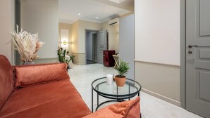 A modern living room with a sofa, a glass coffee table, and decorative plants. - Alegrand Suites (Rhodes)
