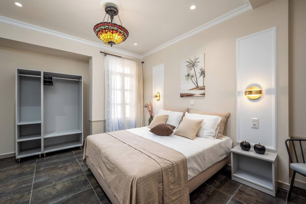 A bedroom with a large bed, a wardrobe, a chandelier, a painting, and a nightstand.