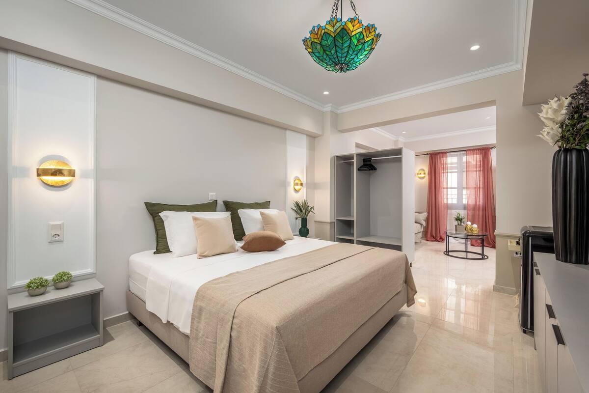 A modern bedroom with a large bed, bedside tables, a chandelier, and a view into an adjacent room.