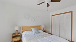 A bedroom with a bed, bedside lamps, a ceiling fan, a wardrobe, and decorative wall art.