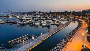 A marina with multiple boats docked, a wooden pier, and a well-lit walkway along the water.