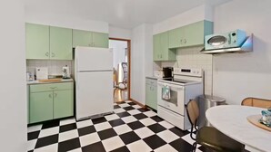 A compact kitchen with green cabinets, a black and white checkered floor, a refrigerator, an oven, and a microwave.