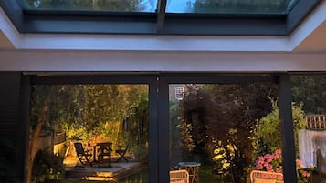 A conservatory with a glass ceiling, outdoor furniture, and a garden view.