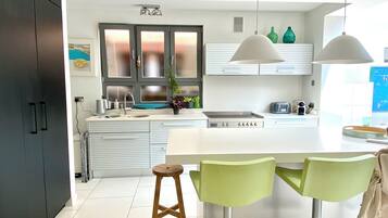 A modern kitchen with a central island, two bar stools, a sink, and a window with frosted glass panels.