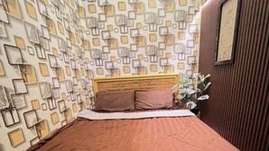 Ein Schlafzimmer mit gemusterten Wänden, einem Holz-Kopfteil, einer braunen Bettdecke und einer Zimmerpflanze.