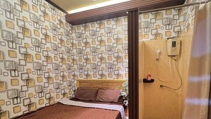 Ein Schlafzimmer mit Bett, Duschbereich und Wand mit geometrischem Muster.
