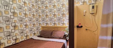 A bedroom with a bed, a shower area, and a wall with a geometric pattern.