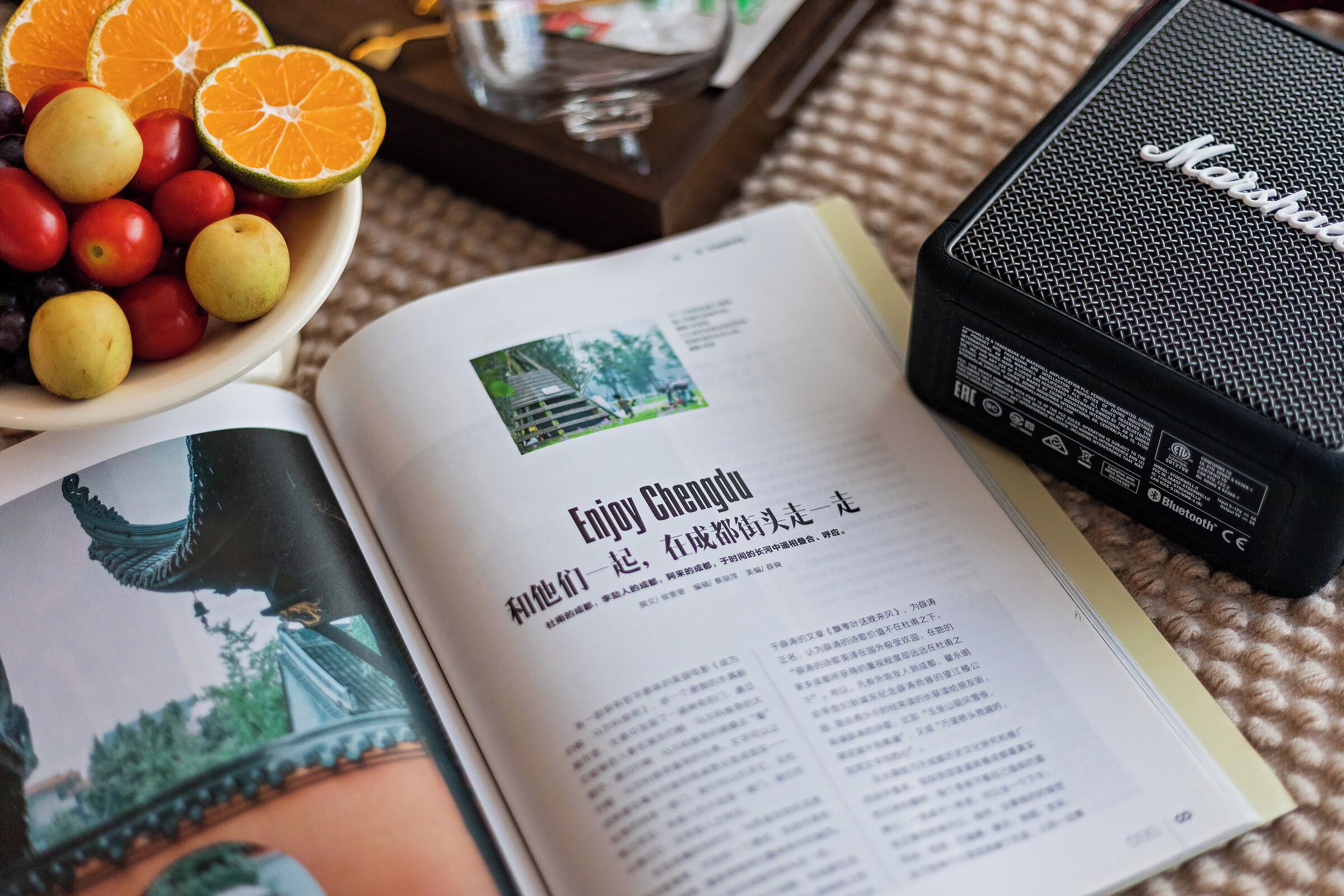 A book open to a page with a travel article and a bowl of fruit on a table.