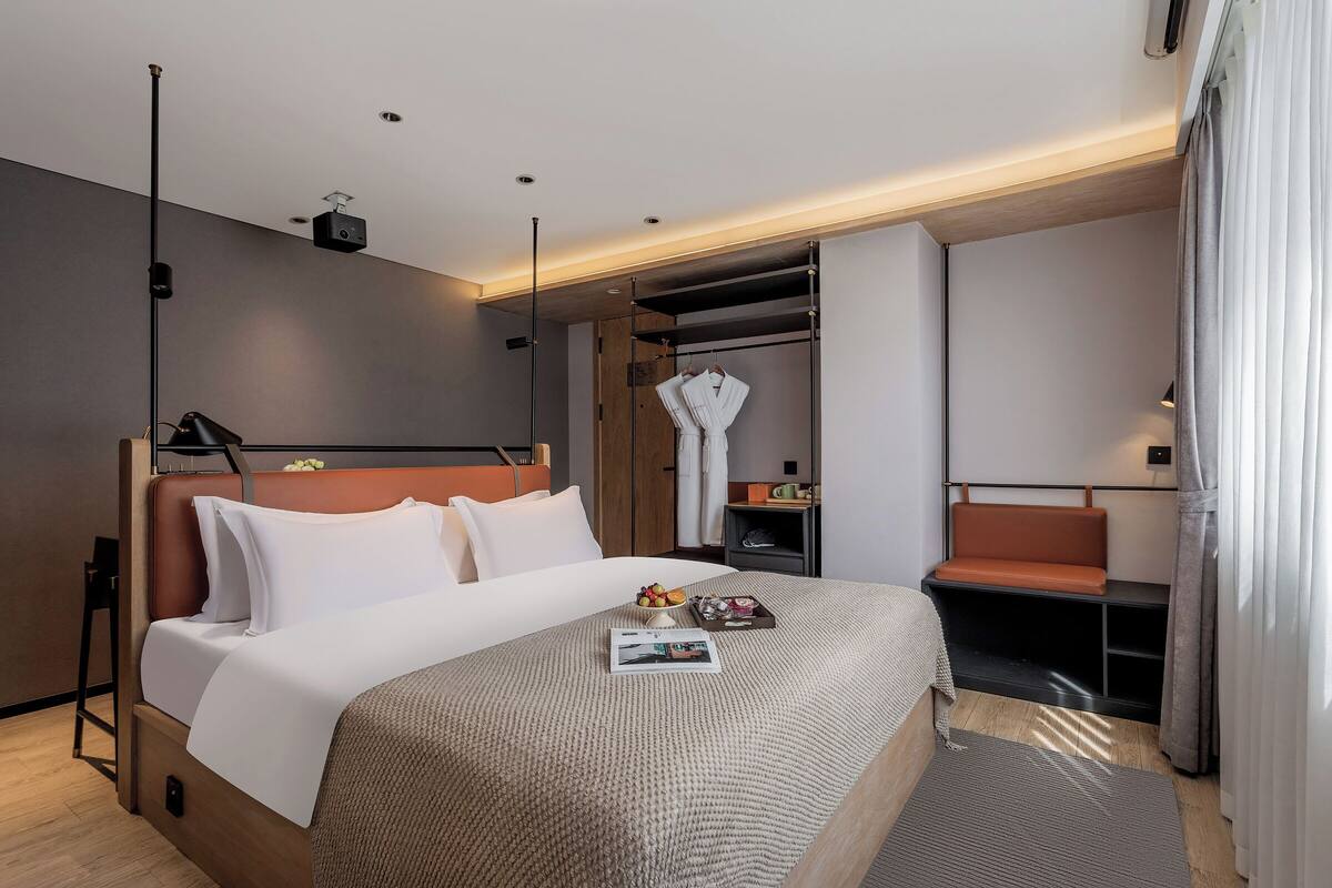 A modern hotel room with a large bed, a seating area, and a wardrobe.