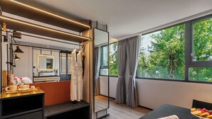 A modern hotel room with a large window, a mirror, a desk with a newspaper, and a side table with toiletries. - Cheens Hotel (Chengdu)