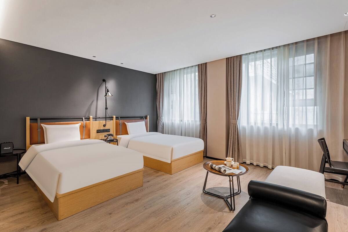 A hotel room with two beds, a desk, a chair, and a lamp.