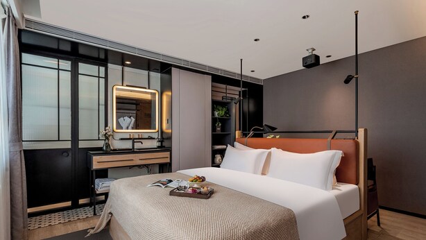A modern hotel room with a large bed, a bedside table, a mirror, a dresser, and a small plant. - Cheens Hotel (Chengdu)