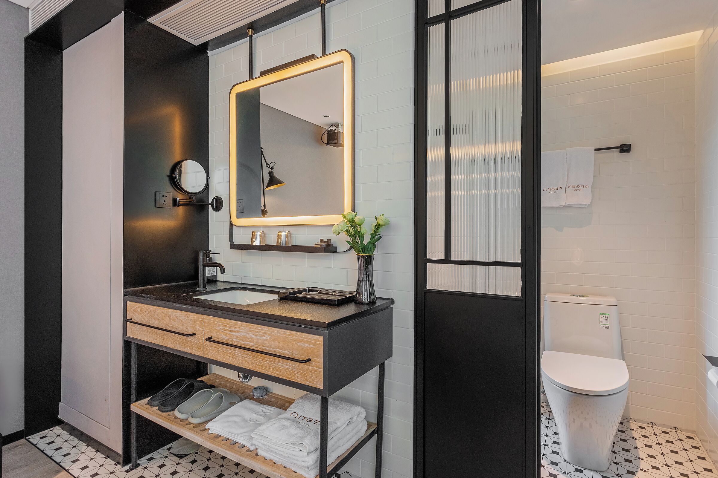 A modern bathroom with a black and white tiled floor, a wooden vanity with a mirror, a sink, and a toilet.