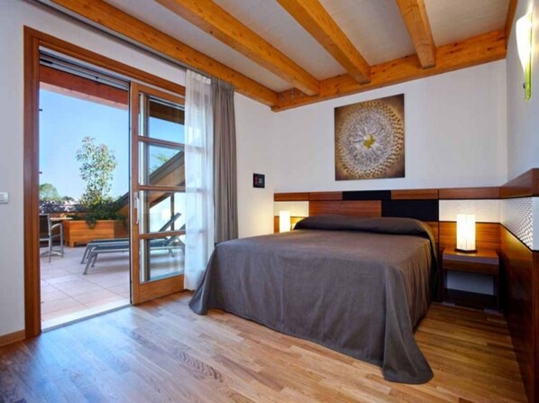 A bedroom with a bed, wooden ceiling beams, a window with a view, and a wall-mounted artwork.