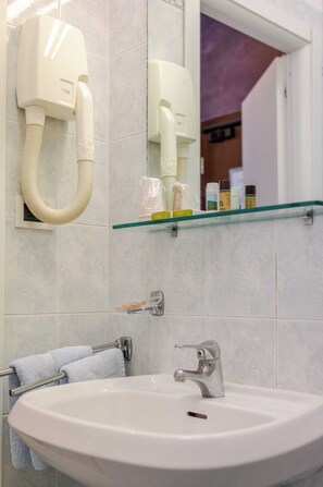 Une salle de bain avec un lavabo blanc, un miroir, un porte-serviettes et une étagère en verre où sont rangés les articles de toilette.