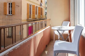 Un balcon avec une balustrade, une table avec des chaises et une fenêtre avec des stores.