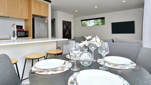 A modern dining area with a table set for four, a kitchen in the background, and a grey sofa. - Modern Comfort in 2-Bedroom Townhouse in Phillipstown (Christchurch)