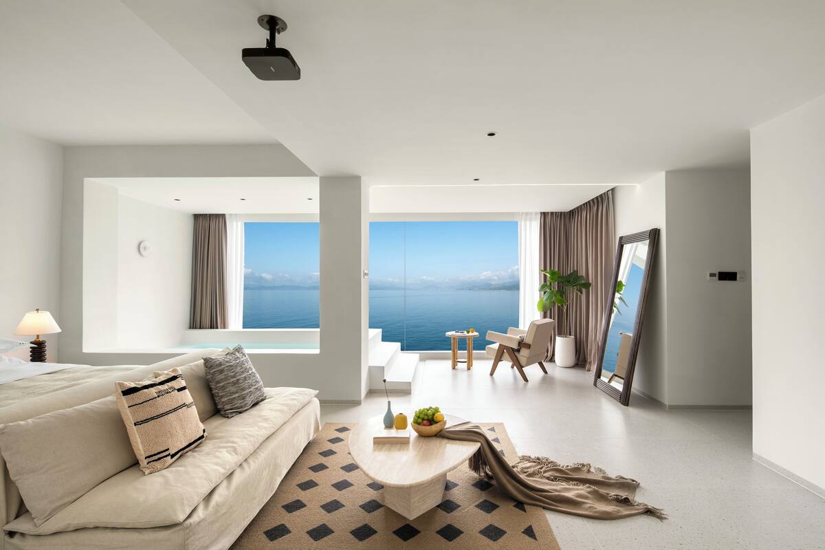 Una camera d'albergo moderna con un ampio balcone, un divano, un tavolino da caffè e vista sul mare.