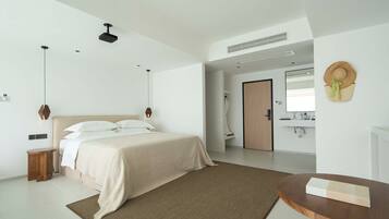 A modern bedroom with a large bed, bedside tables, a wooden nightstand, a round wooden table, and a wall-mounted hat.
