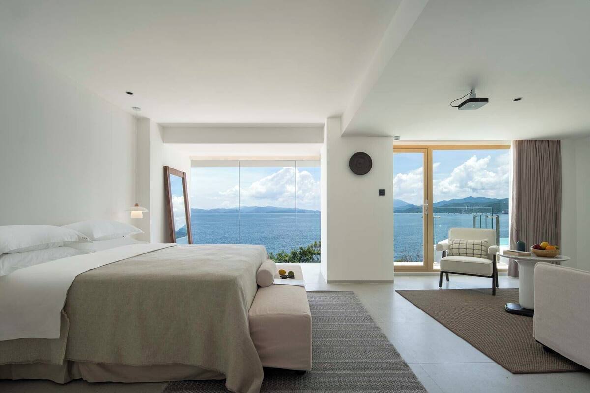 Una camera da letto moderna con un letto grande, un'area salotto vista mare e un balcone con vista sul mare e sulle montagne.