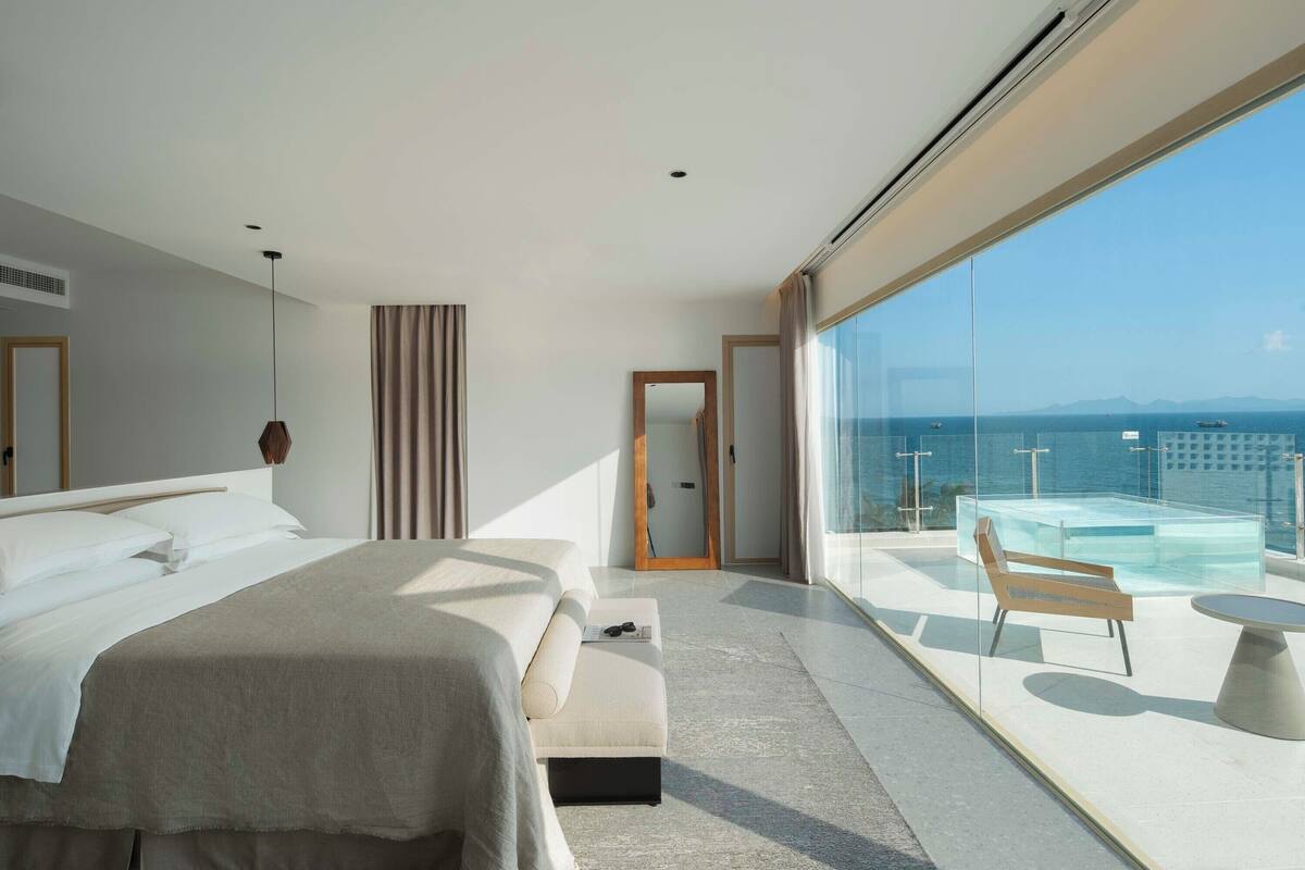 Camera d'albergo moderna con un letto grande, un angolo relax vista mare e un balcone con vetrate.