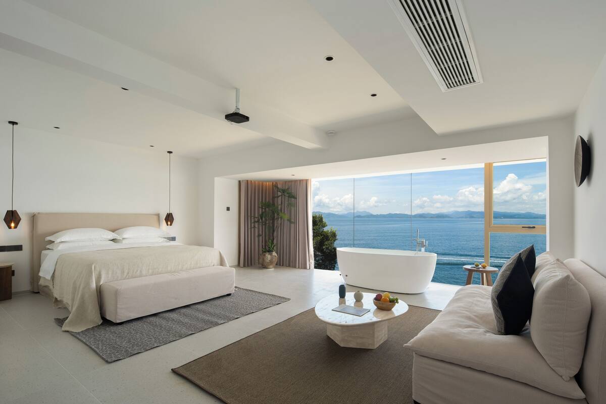 Una camera moderna con un letto grande, una poltrona, un tavolino rotondo e vista sul mare.