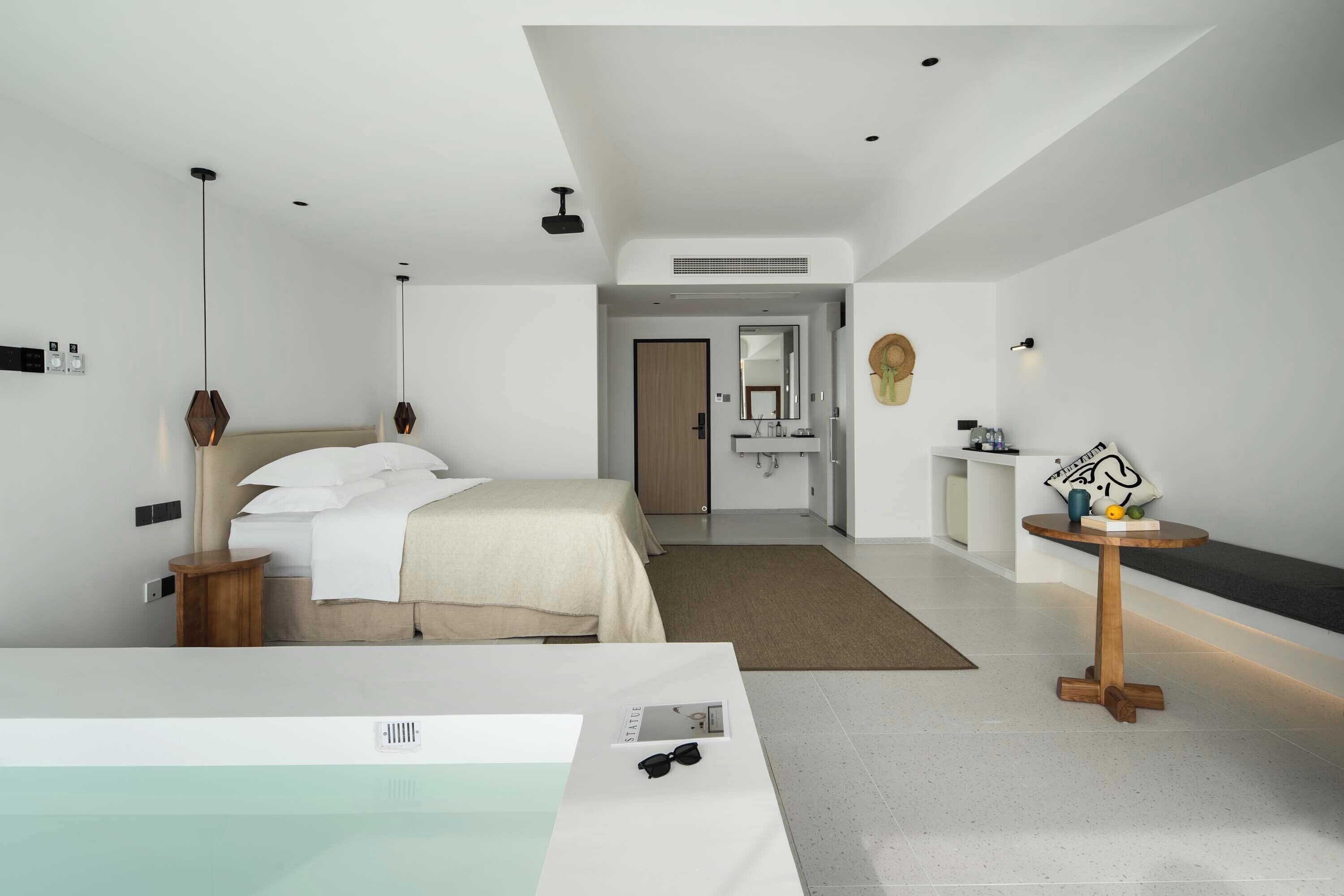 Ett modernt hotellrum med en stor säng, ett litet runt bord, ett badrum med en spegel och utsikt över hallen.