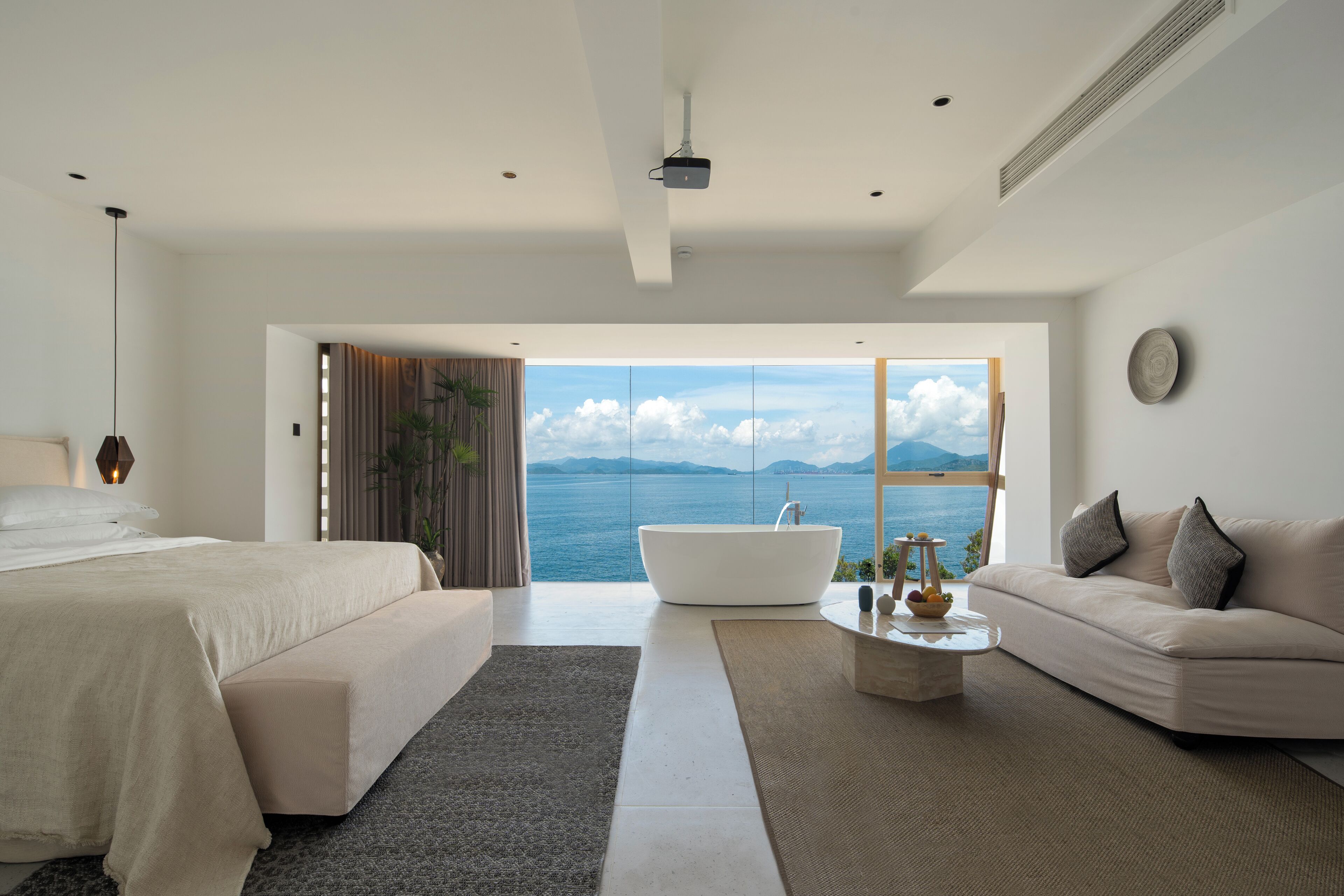 A modern bedroom with a large bed, a sitting area with a sofa, and a bathtub.