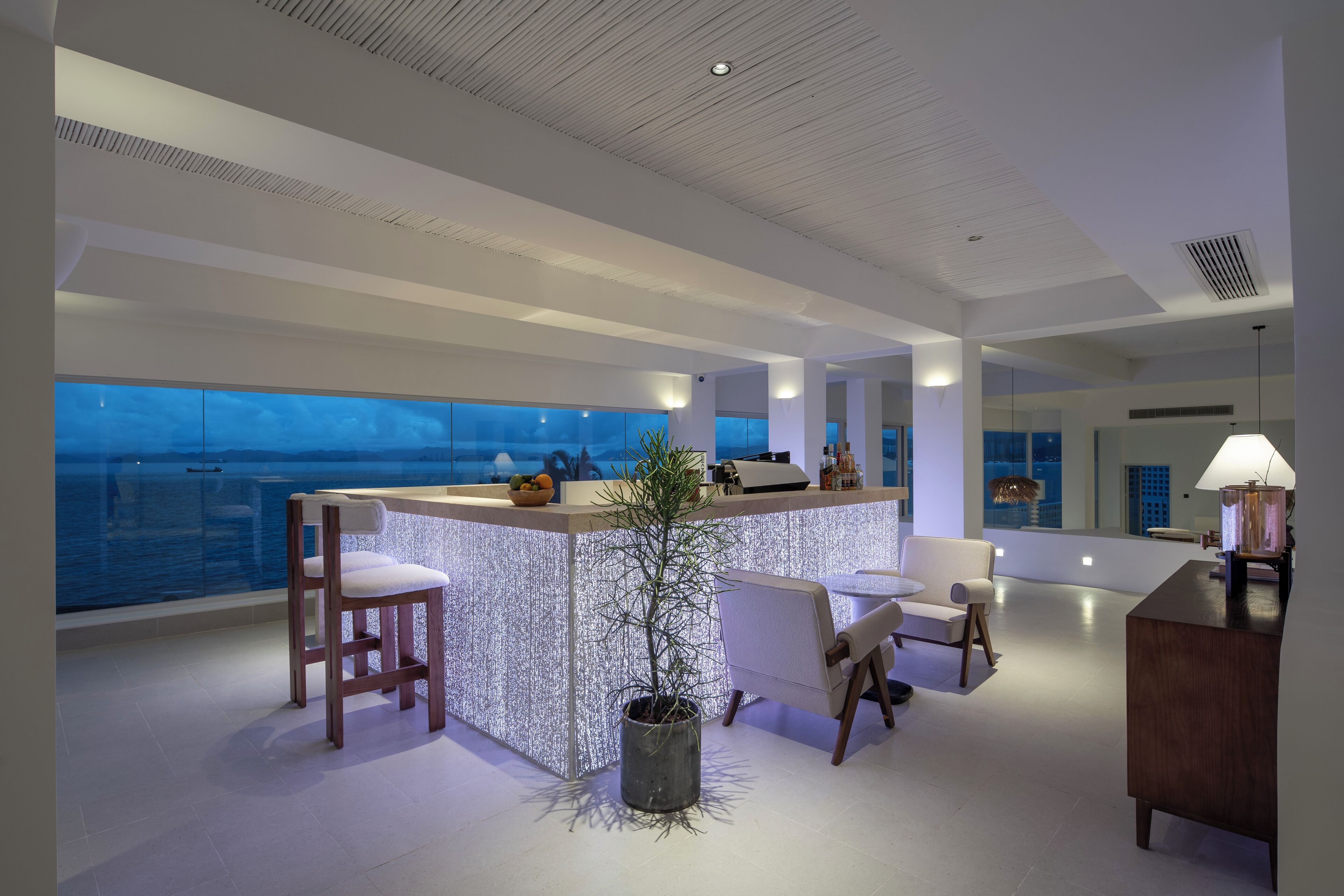 A modern interior with a bar area, seating, and a large window overlooking the sea.
