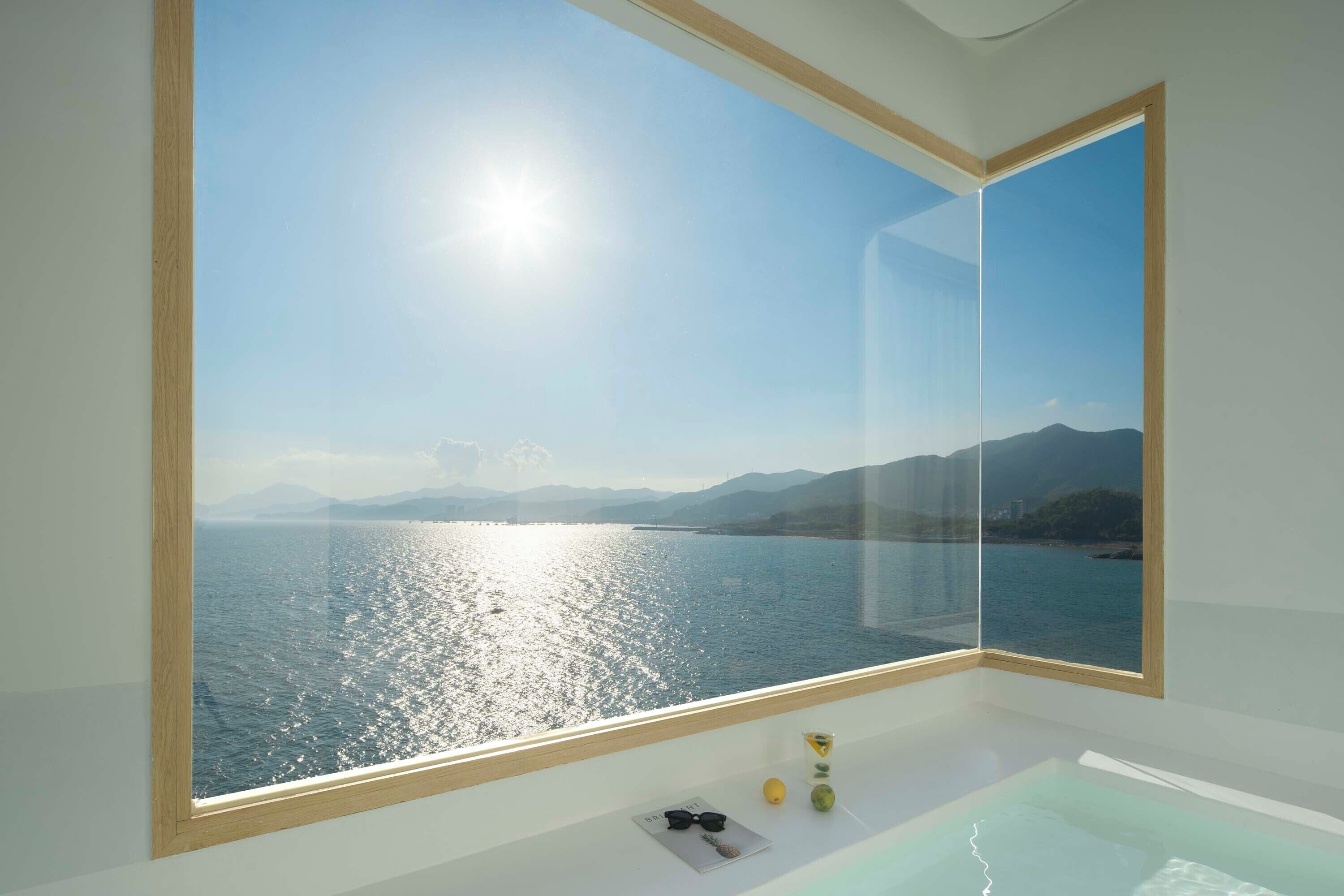 A modern bathroom with a large window offering a view of a calm sea and distant mountains.